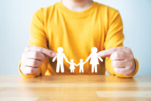 hand protecting family on wood table. healthcare and life insurance concept